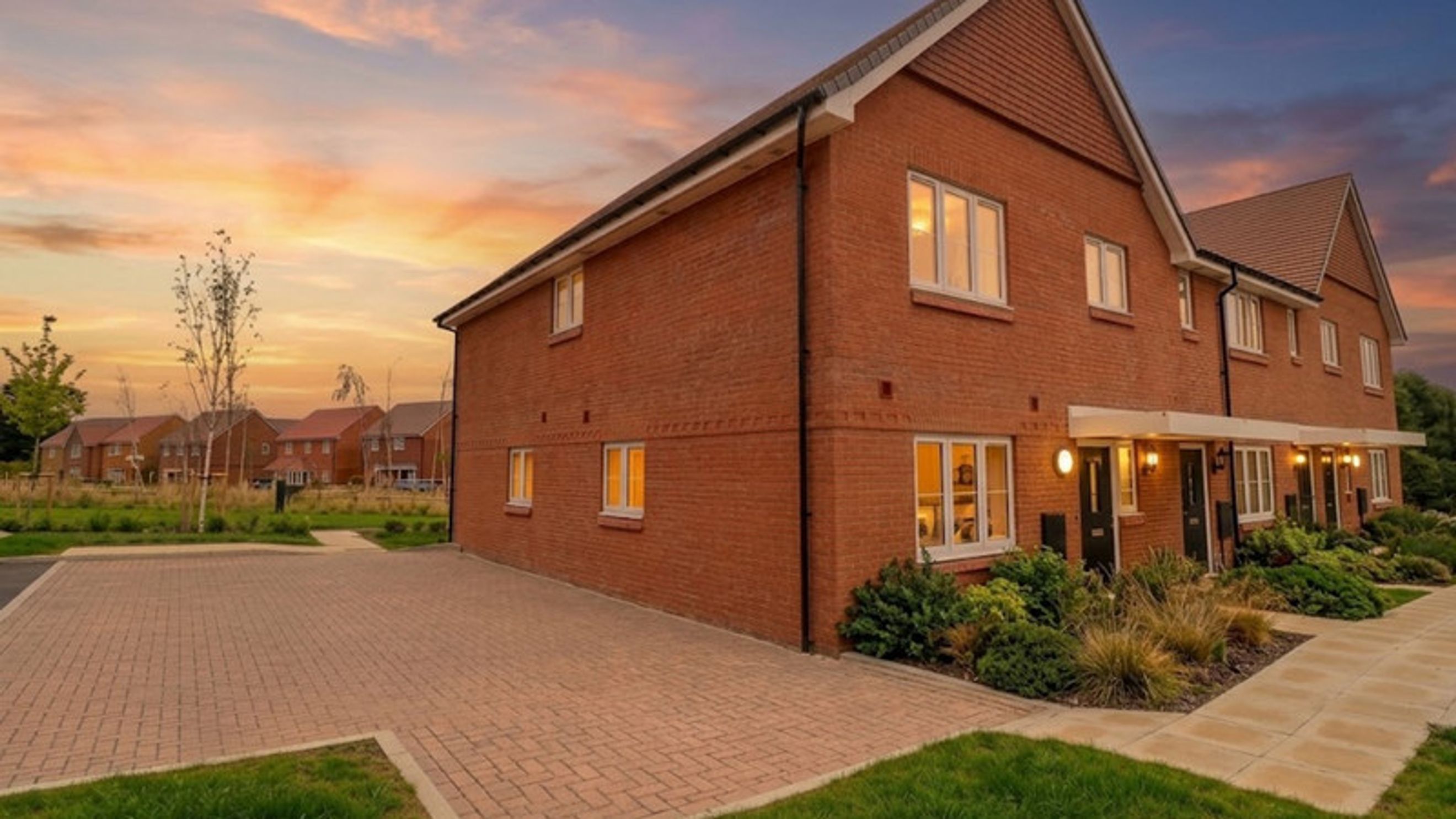 A row of brick townhouses with white-trimmed windows and landscaped front yards under a sunset sky.