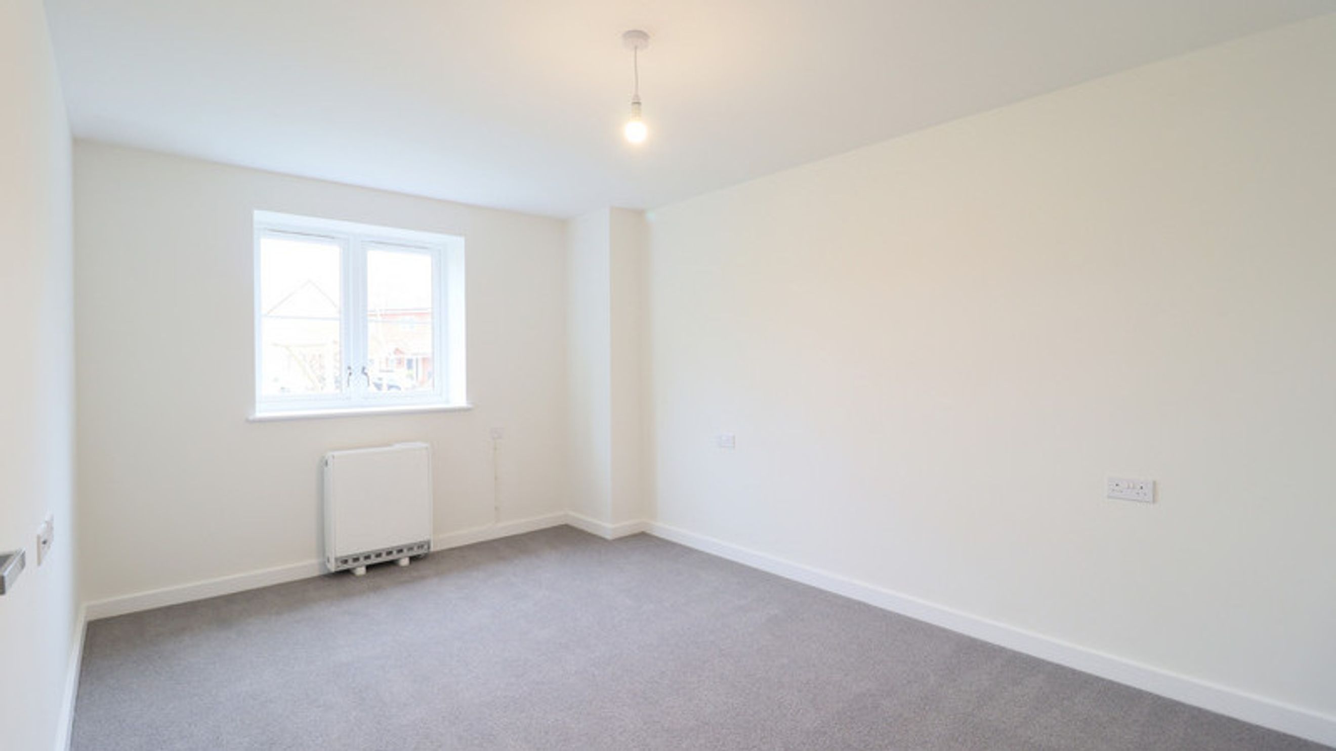 A room with a window, radiator, and carpet.