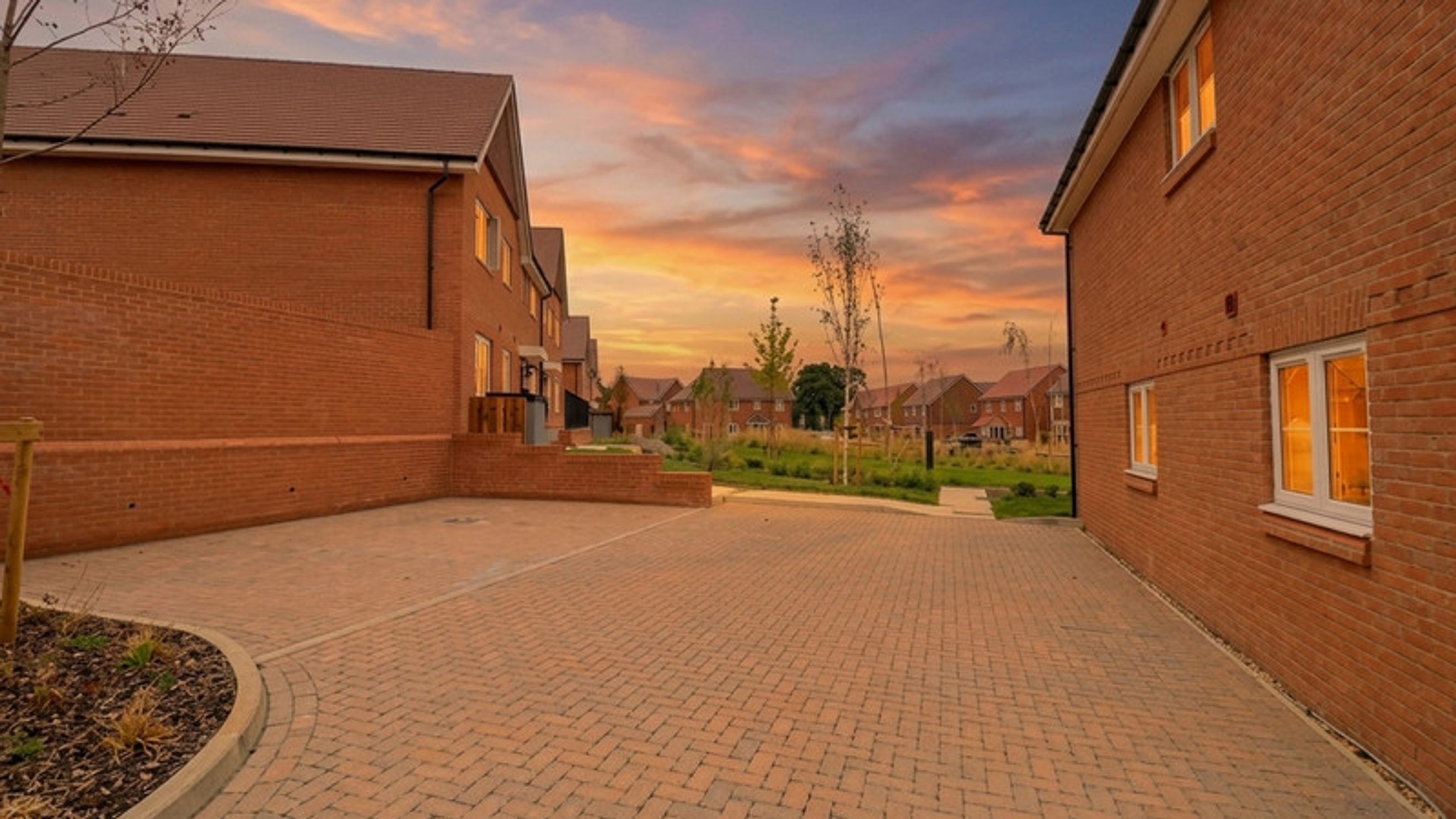 A paved driveway in front of brick houses with a sunset sky.