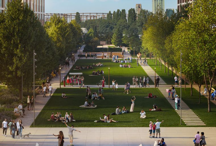 A park with people relaxing on the grass and walking on paths, with modern buildings in the background and a fountain in the foreground.