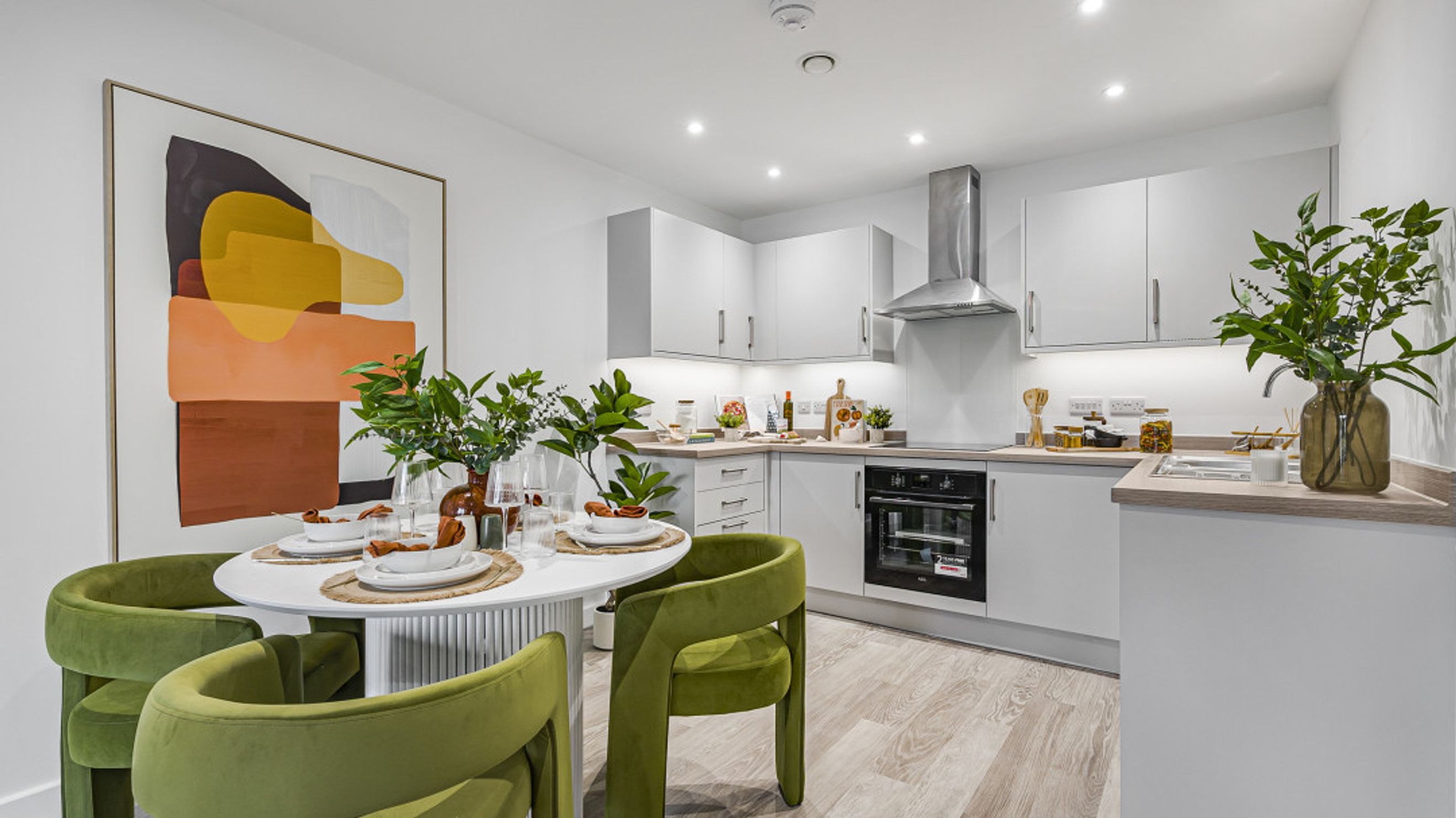 A modern kitchen and dining area with a round table, green chairs, and abstract art.