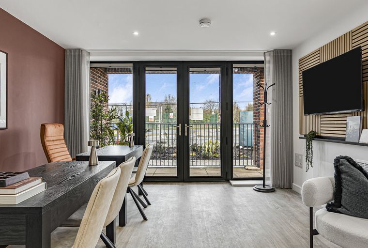 A dining area with a table and chairs next to large glass doors and a living area with a TV mounted on a wooden wall panel.
