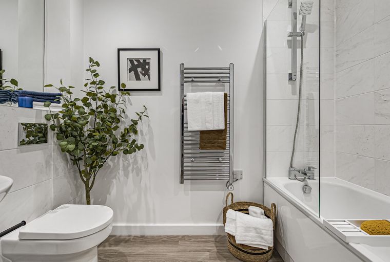 A modern bathroom with a toilet, bathtub, shower, and heated towel rail.