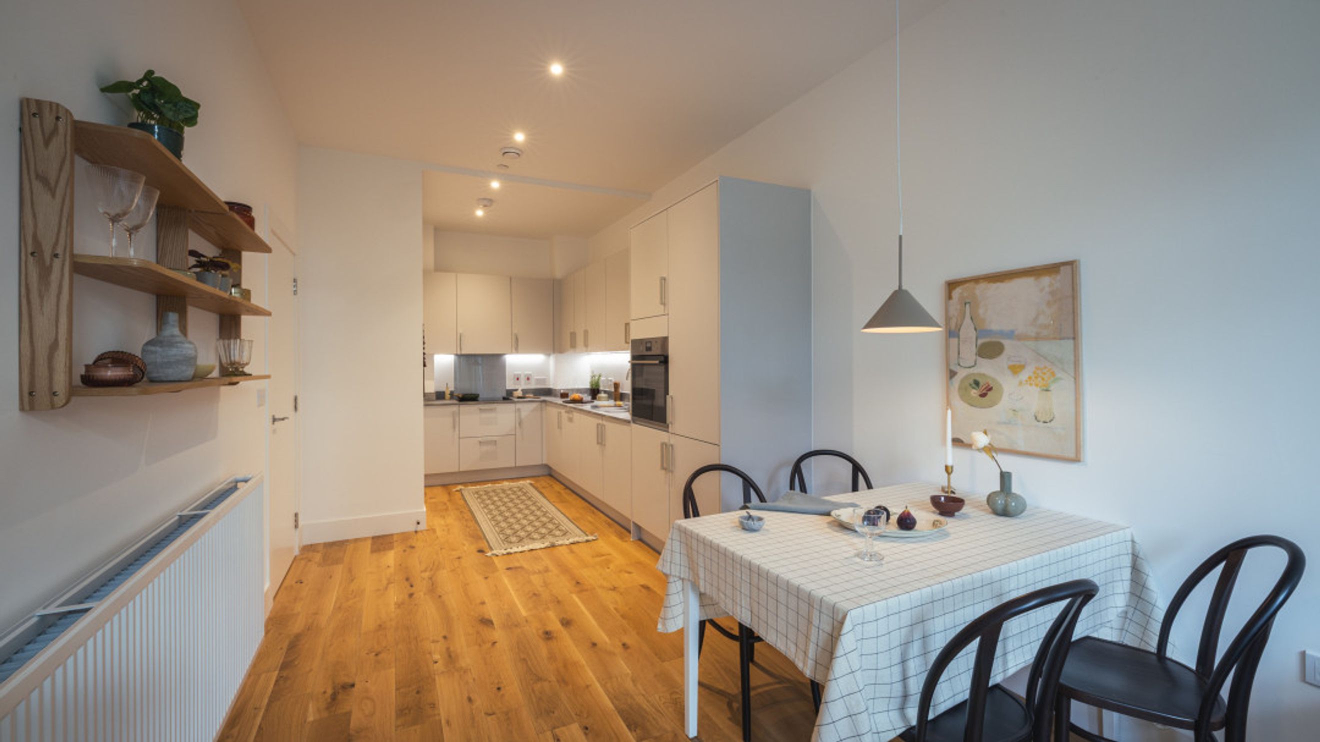 A dining area and kitchen with wooden floors and white cabinets.