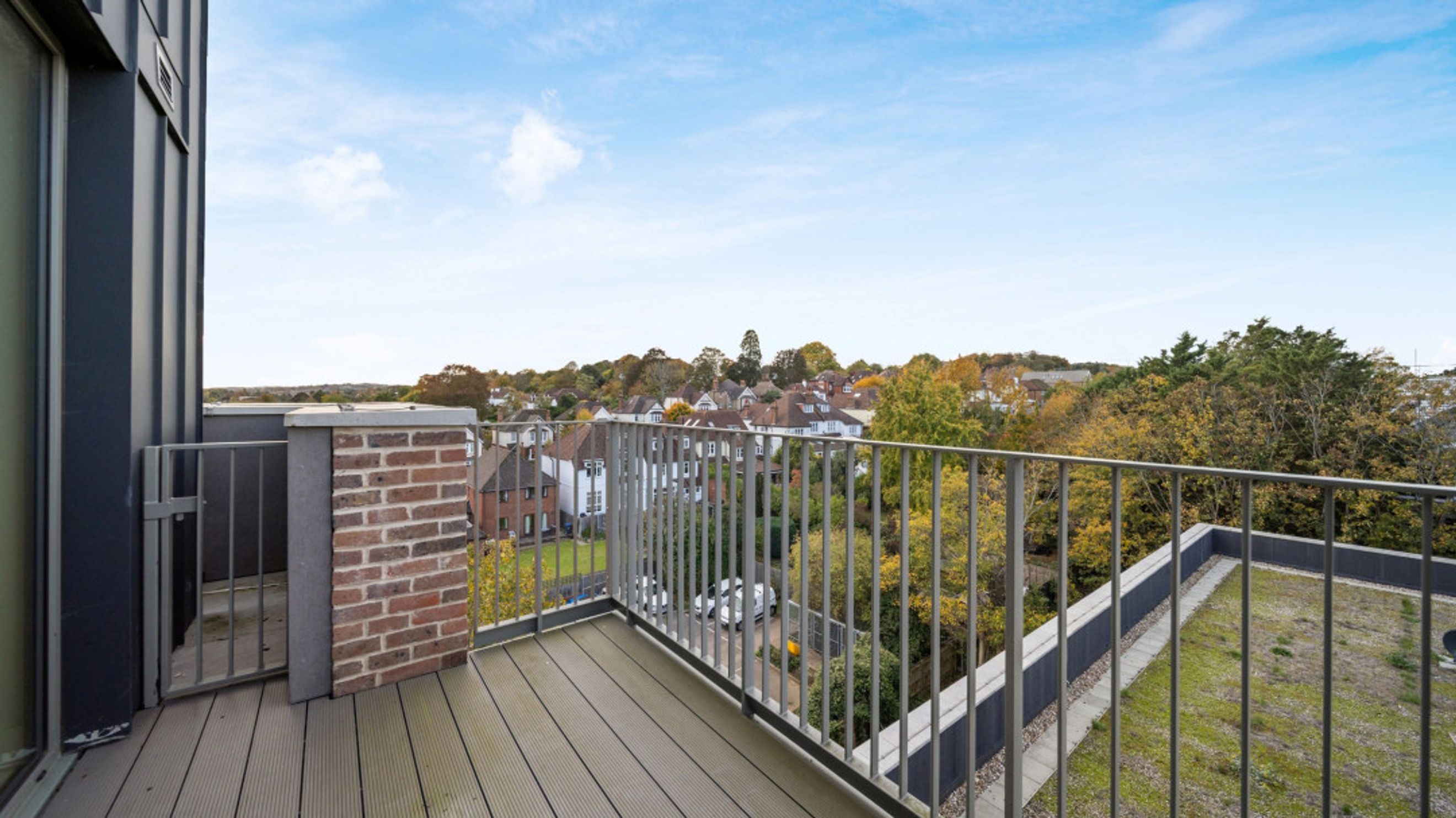 A balcony with a view of houses and trees under a blue sky.