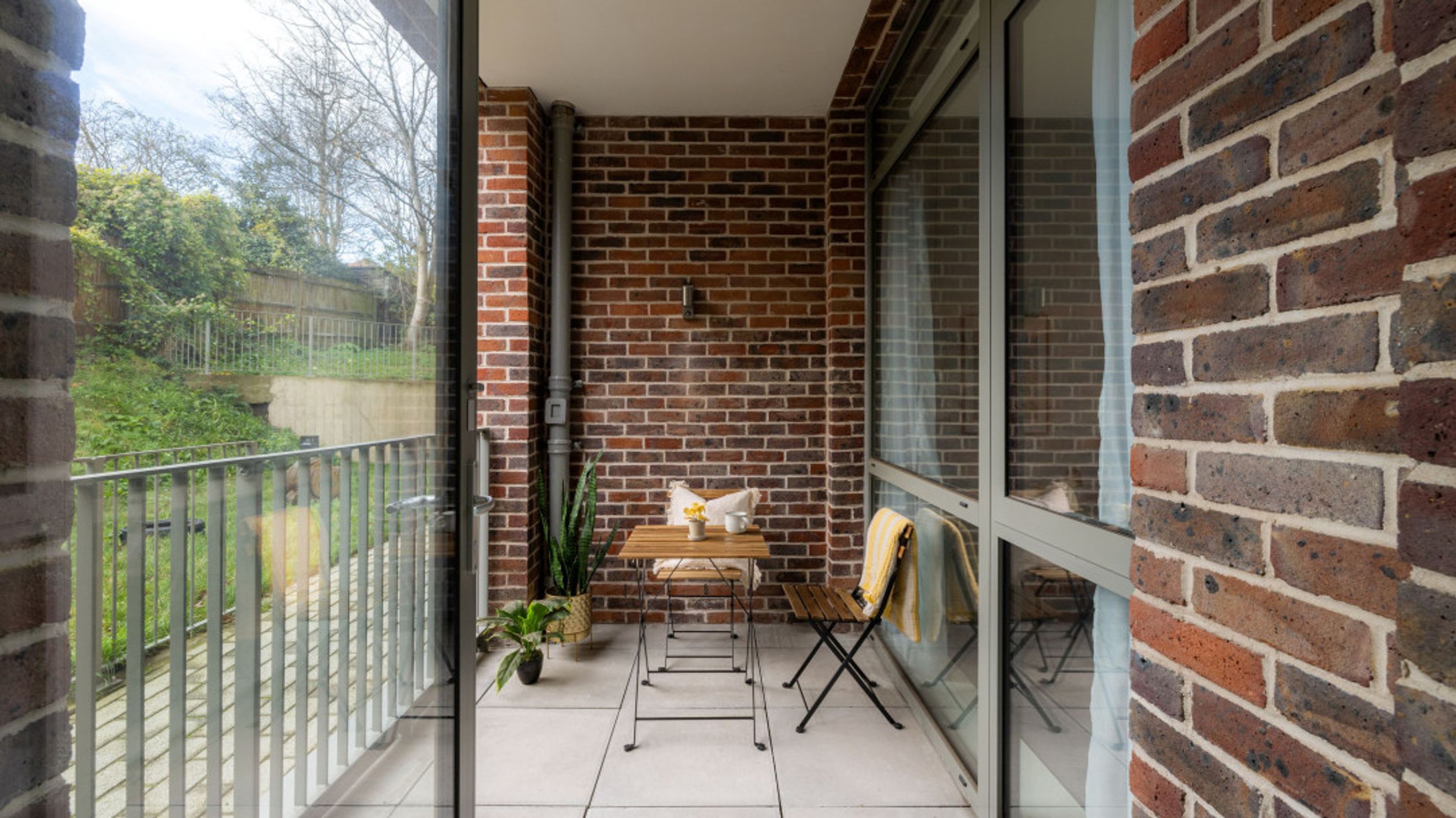 A balcony with a small table and chairs, overlooking a garden area.