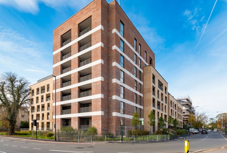 A modern brick apartment building with balconies and windows under a blue sky.