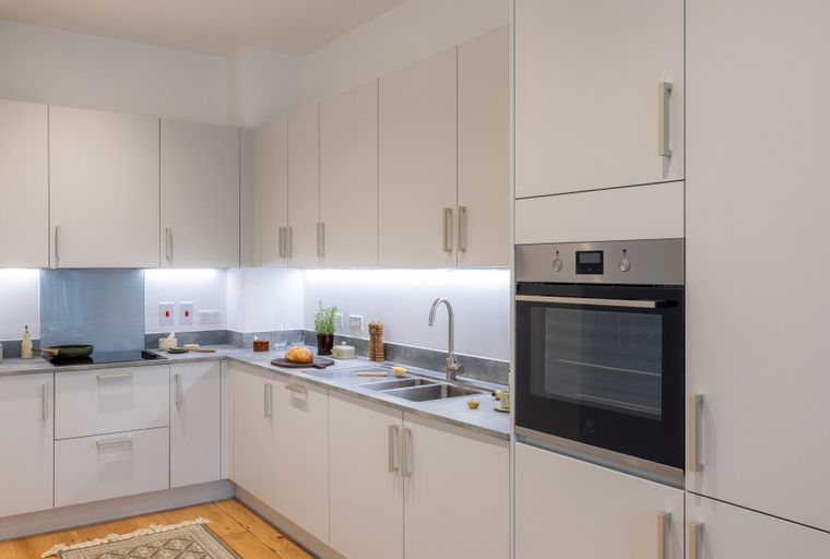 A modern kitchen with white cabinets, a built-in oven, and a double sink.
