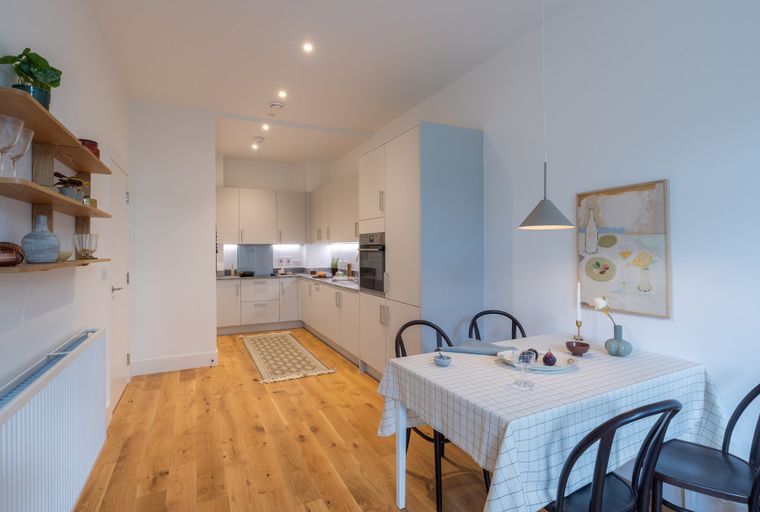 A dining area and kitchen with white cabinets, a dining table with chairs, and wooden flooring.
