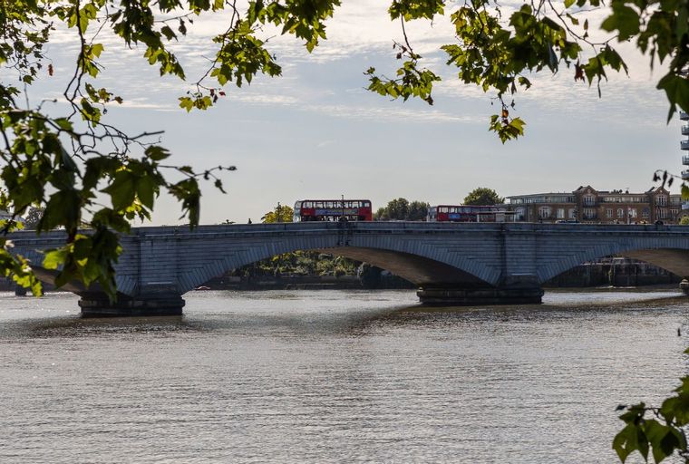 A bridge over a body of water with red double-decker buses on it.