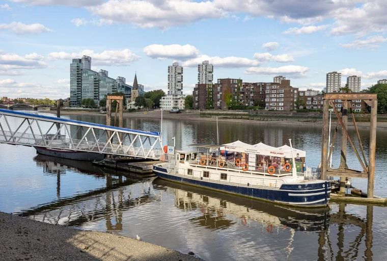A boat docked at a pier on a river with buildings in the background.