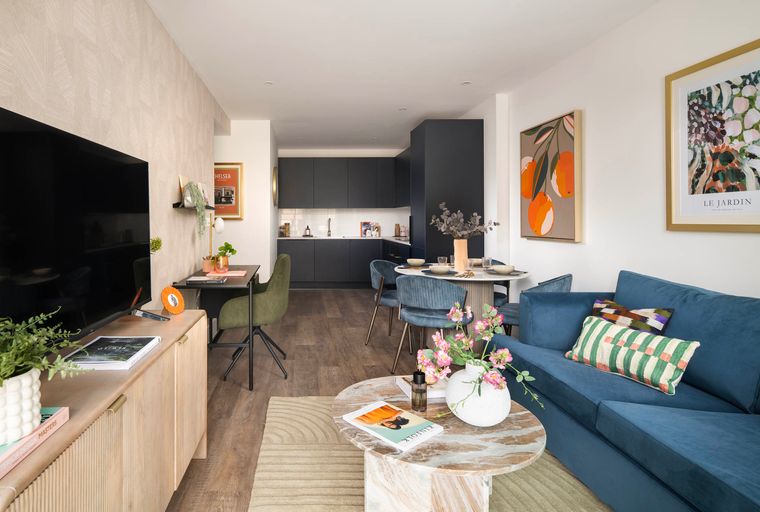 A living room and kitchen area with a sofa, coffee table, dining table, and kitchen cabinets.