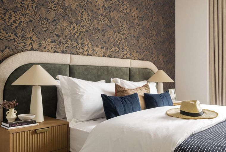 A bedroom with a bed, nightstand, and patterned wallpaper.