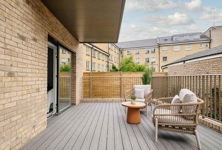A balcony with two chairs, a table, and a wooden fence.