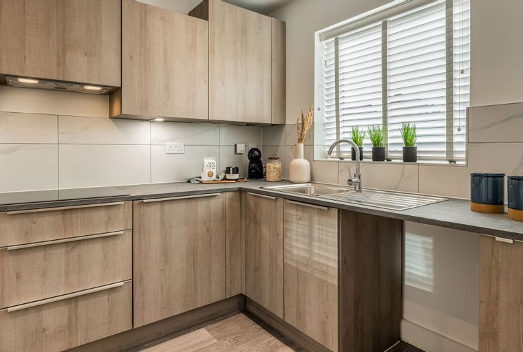 A kitchen with light wood cabinets, a sink, and a window with blinds.
