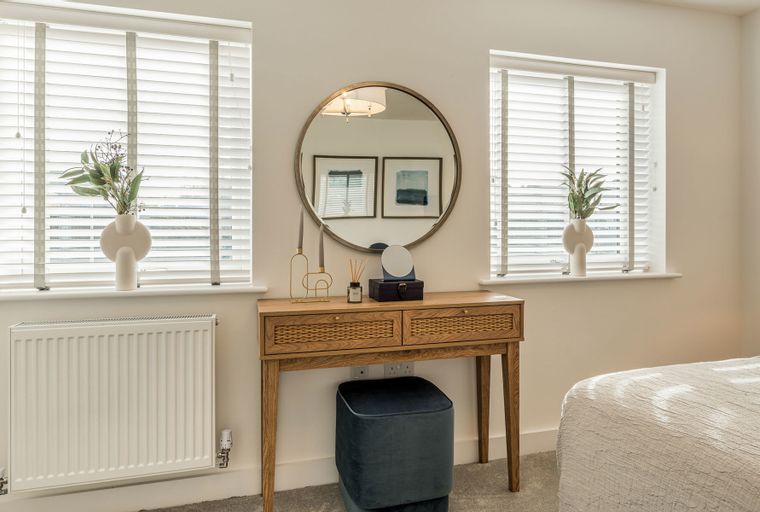 A bedroom with a vanity table, a mirror, and two windows with blinds.