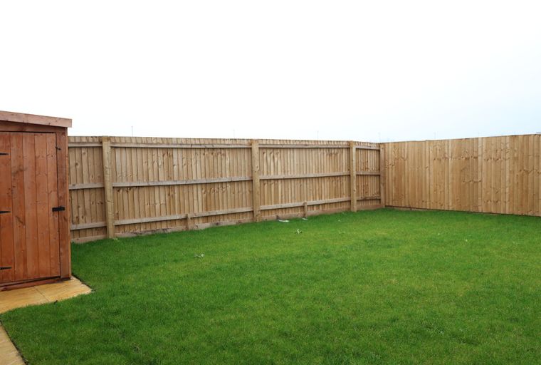 A backyard with a wooden shed, a lawn, and a wooden fence.