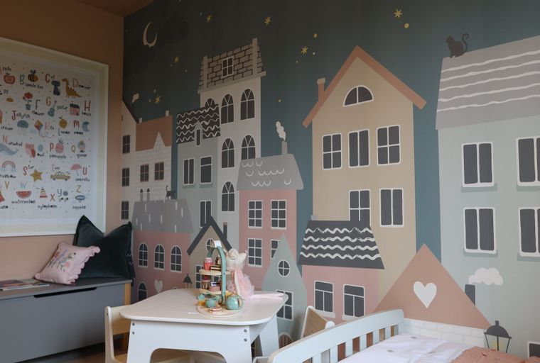 A children's room with a mural of houses, a table, chairs, and a storage bench.