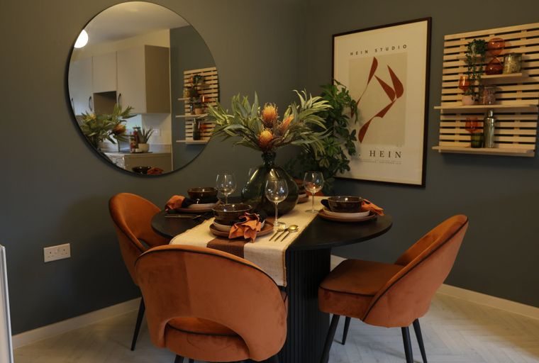 A dining table with four orange chairs, a vase of flowers, and a round mirror.