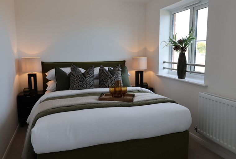A bedroom with a bed, pillows, bedside lamps, and a window.