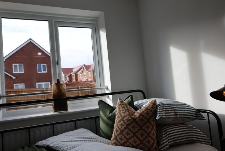 A bedroom with a bed, pillows, a window, and a lamp.