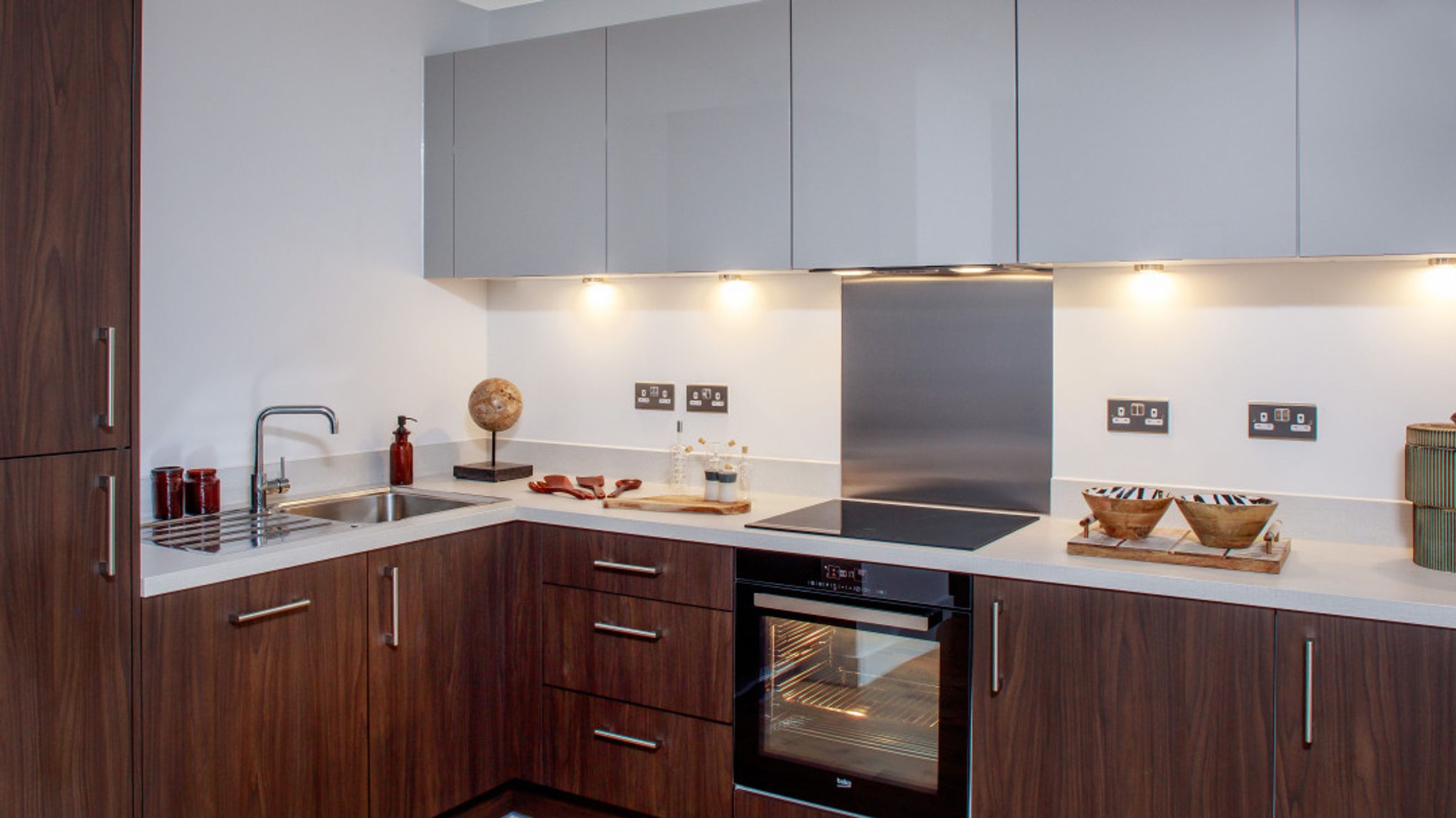 A modern kitchen with dark wood cabinets, a sink, an oven, and an induction hob.