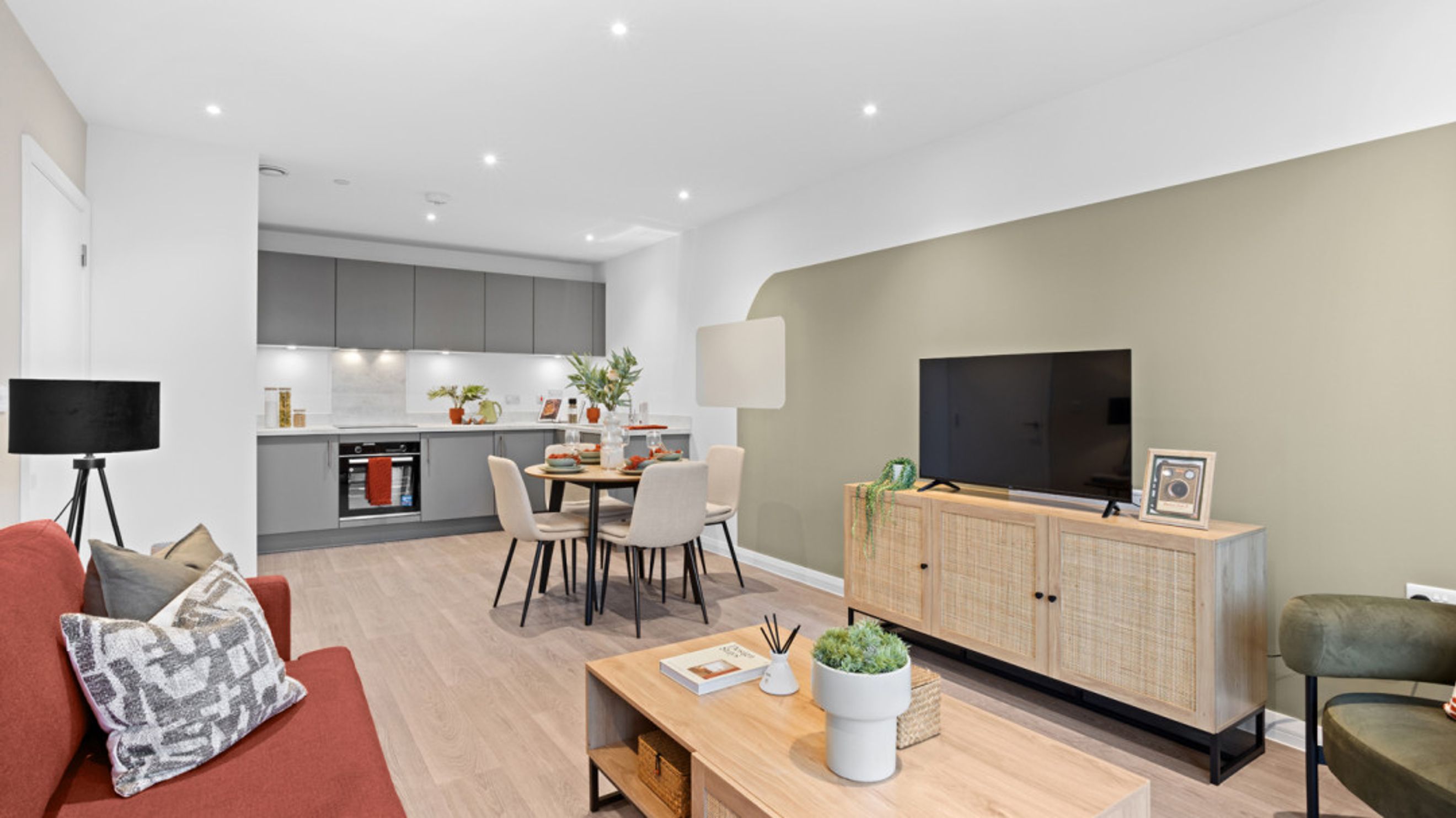A living room and kitchen area with a dining table and chairs, a sofa, a television, and kitchen cabinets.