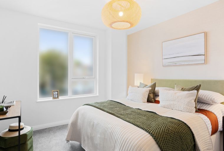 A bedroom with a bed, pillows, a throw blanket, a window, and a vanity table.