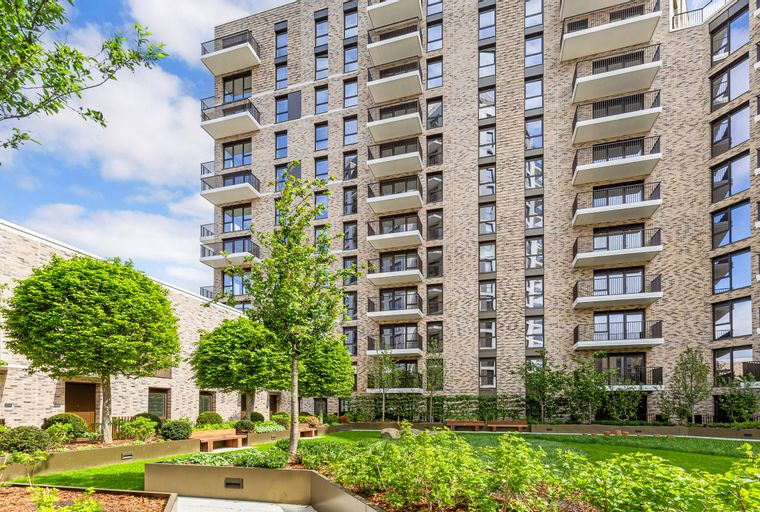 A modern apartment building with balconies overlooking a landscaped courtyard with trees and benches.