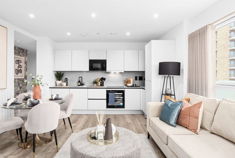 A modern apartment living room and kitchen area with a dining table, sofa, and kitchen cabinets.