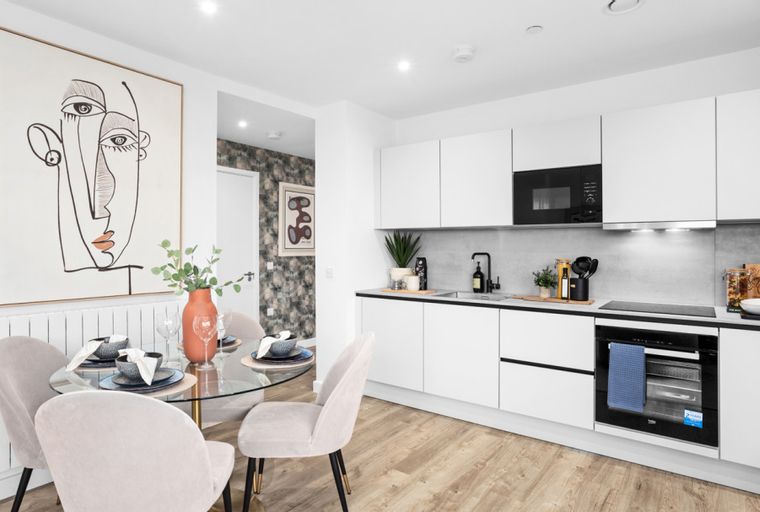 A modern kitchen and dining area with white cabinets, a glass dining table, and abstract art.