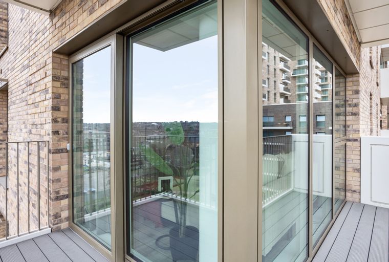 A balcony with large windows overlooking a city view and brick buildings.