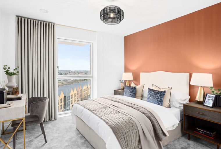A bedroom with a bed, nightstands, a vanity, and a window overlooking a cityscape.