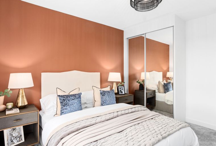 A bedroom with a bed, bedside tables, lamps, and a mirrored wardrobe.