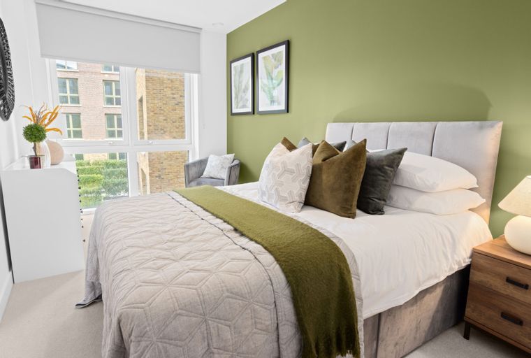 A bedroom with a bed, pillows, a throw blanket, and a nightstand with a lamp.