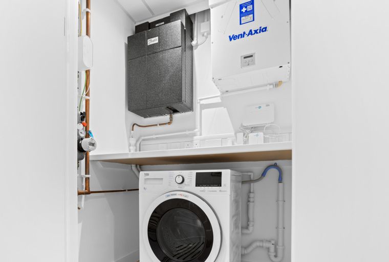 A utility room with a washing machine, ventilation system, and heating unit.