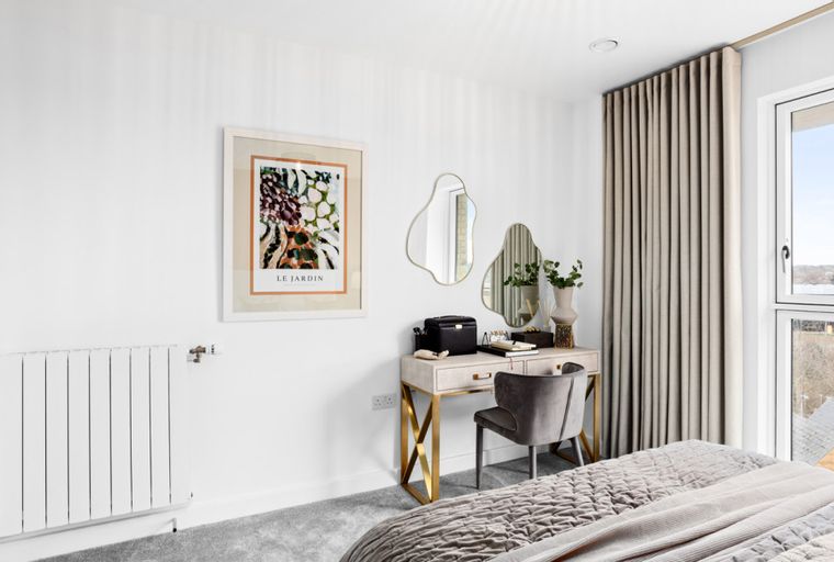 A bedroom with a vanity desk, mirrors, a radiator, and a window with curtains.