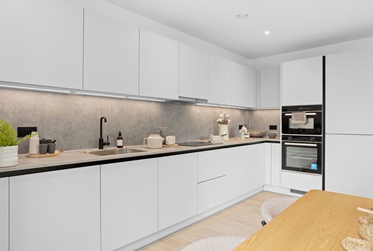 A modern white kitchen with integrated ovens, a sink, and a grey backsplash.