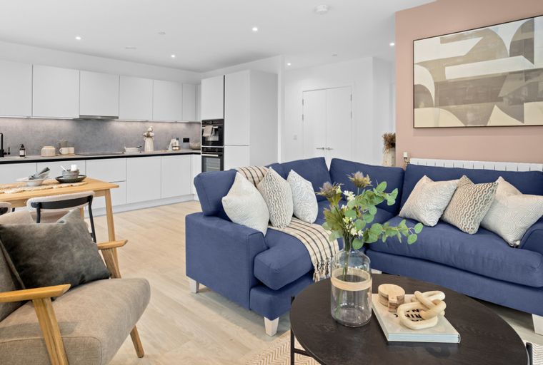A living room and kitchen area with a blue sectional sofa, dining table, and modern kitchen cabinets.