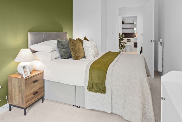 A bedroom with a bed, bedside table, and an open door to a bathroom.