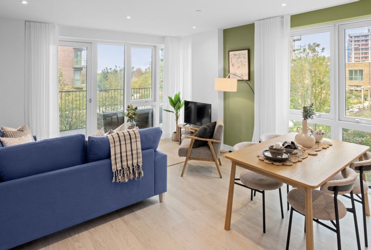 A living and dining room with a blue sofa, a dining table with chairs, and large windows.