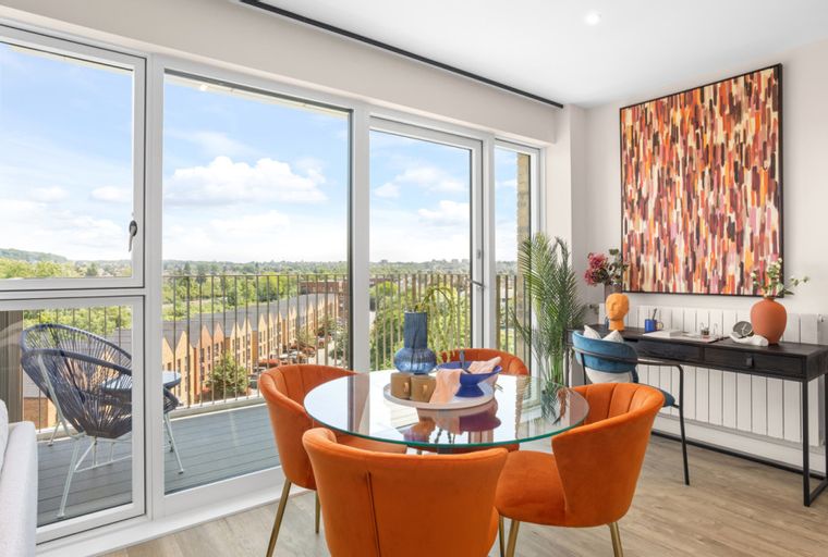 A dining area with a glass-top table, orange chairs, and large windows overlooking a cityscape.