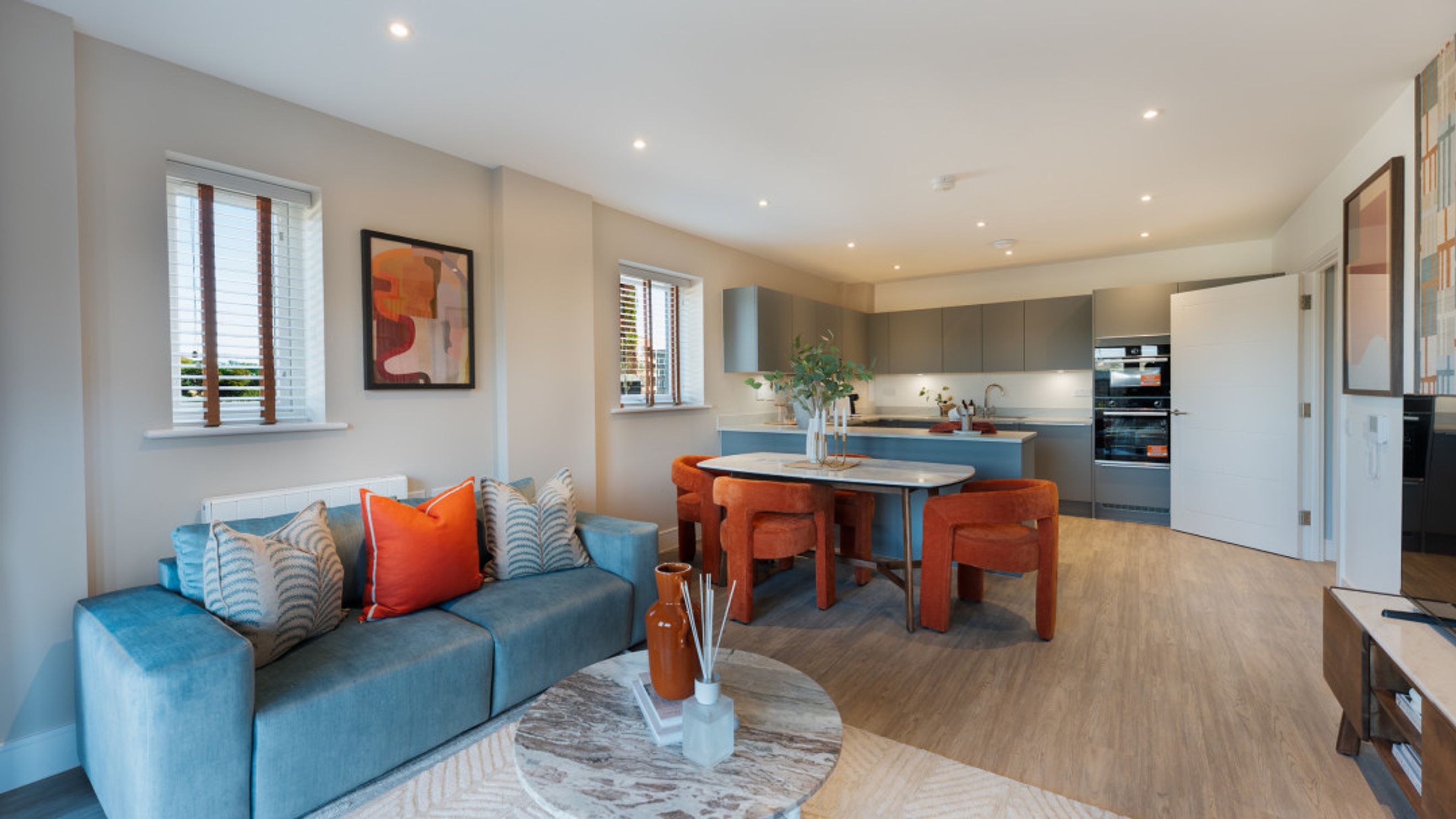 A living room and kitchen area with a blue sofa, orange chairs, and a kitchen island.
