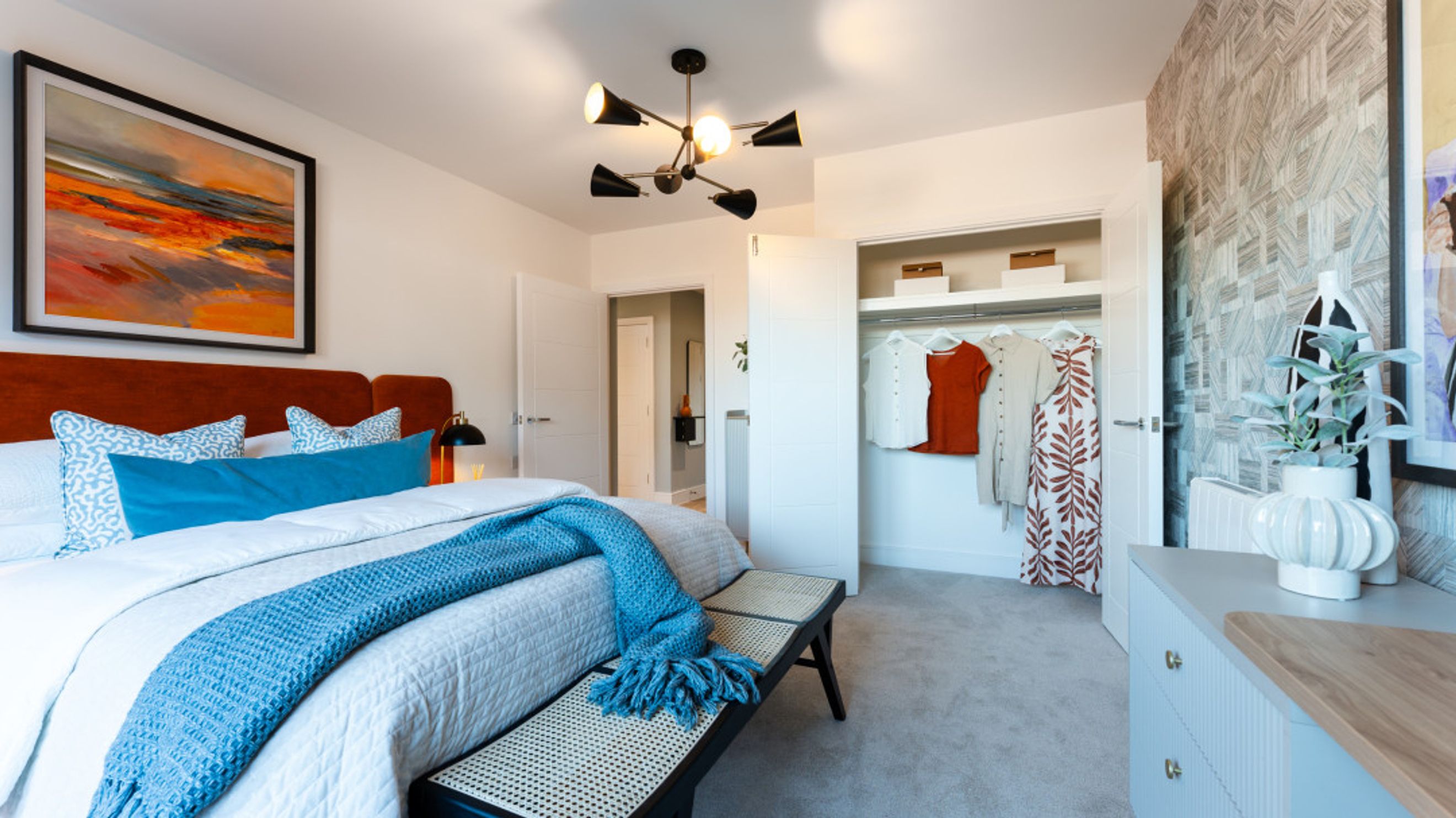 A bedroom with a bed, pillows, a throw blanket, a chandelier, and a closet.