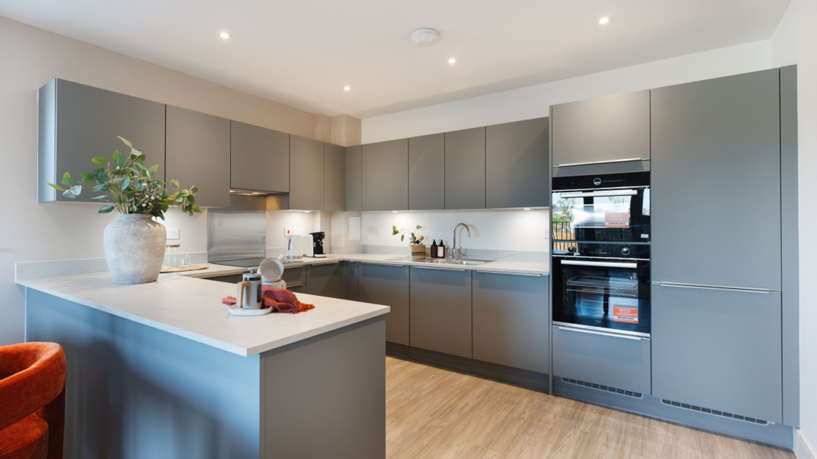 A modern kitchen with grey cabinets, a kitchen island, and integrated ovens.