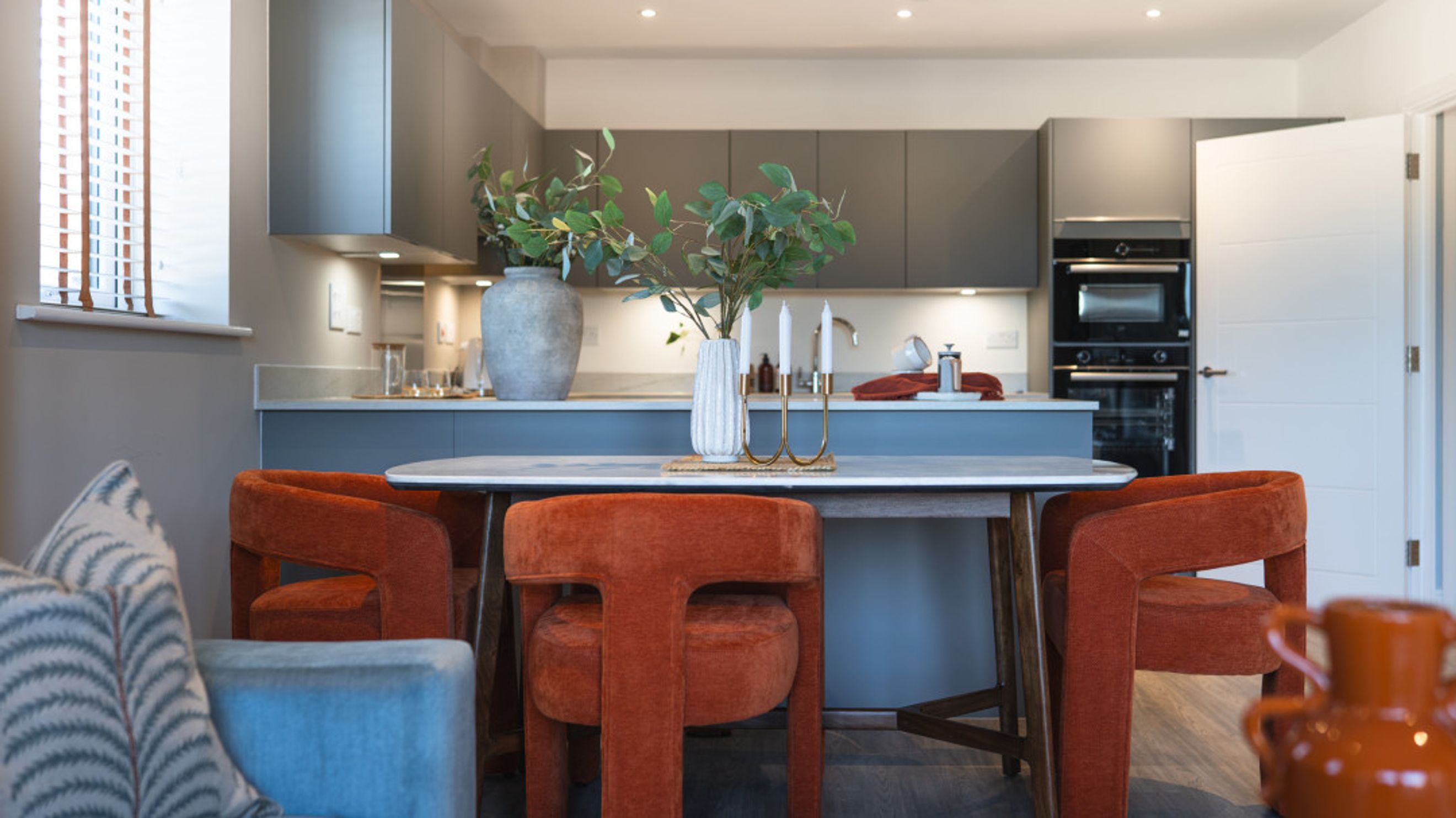 A dining table with orange chairs in front of a kitchen island.