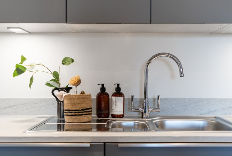 A kitchen sink with a faucet, soap dispensers, and a decorative basket.