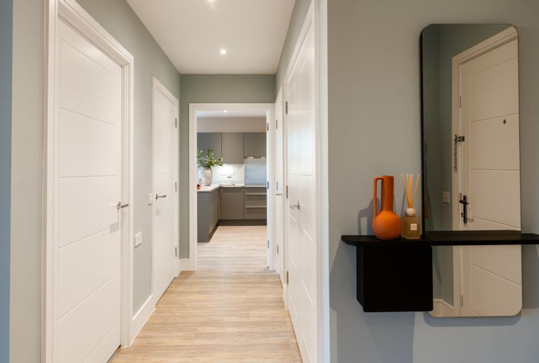 A hallway with white doors, a wood-effect floor, and a view into a kitchen.