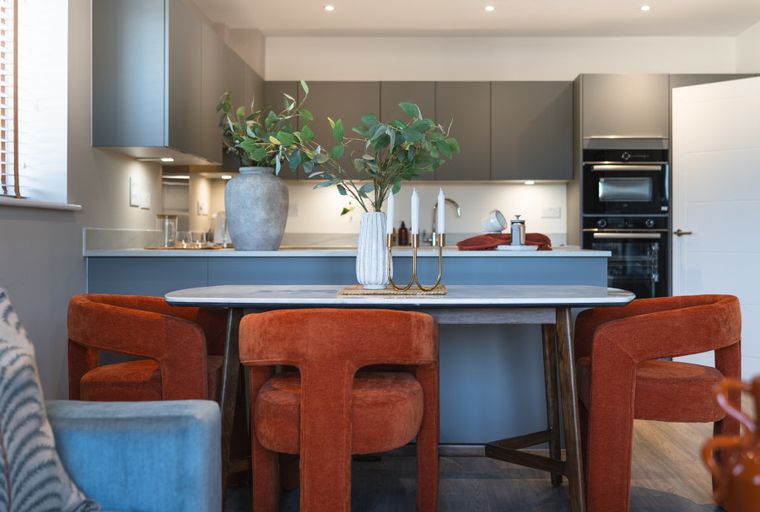 A dining table with orange chairs in front of a kitchen island.