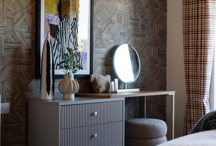 A dressing area with a dresser, vanity table, and lighted mirror.